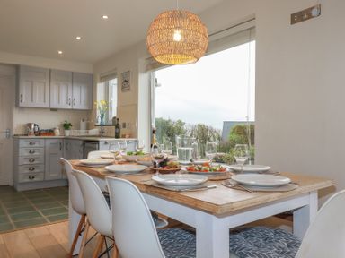 A dining table set with plates glasses and food next to a kitchen with cabinets at Coastmans Nest in Mawgan Porth