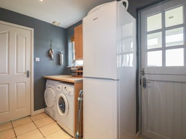 A utility room with a washing machine dryer refrigerator wooden countertop and a door with glass panes at Coastmans Nest in Mawgan Porth