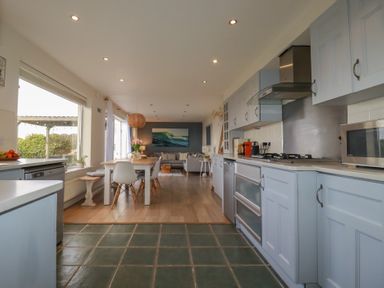 A kitchen with light blue cabinets and dining table with chairs next to a living area at Coastmans Nest in Mawgan Porth