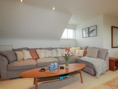 A living room with a grey sectional sofa and a wooden coffee table with flowers and tea set at Coastmans Nest in Mawgan Porth
