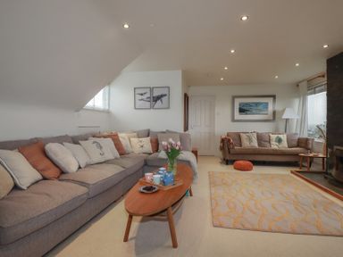 A living room with two sofas a wooden coffee table with flowers and cups and framed pictures on the walls at Coastmans Nest in Mawgan Porth