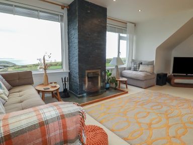 A living room with sofas a fireplace windows with views and a patterned rug at Coastmans Nest in Mawgan Porth