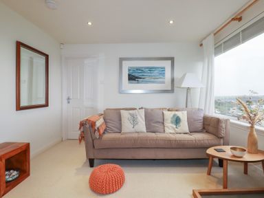 A living room with a sofa and cushions a lamp a window and a small wooden table at Coastmans Nest in Mawgan Porth