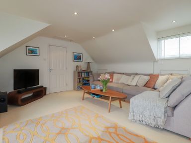 A living room with a large sofa and a coffee table with flowers in a vase at Coastmans Nest in Mawgan Porth