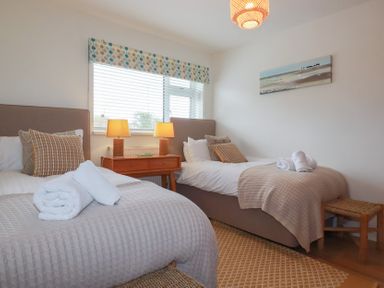 A bedroom with two single beds a wooden nightstand with two lamps a window and a wall painting at Coastman's Nest in Mawgan Porth