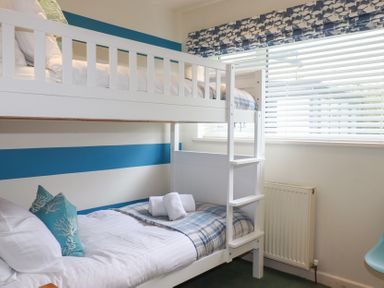 A bedroom with a white bunk bed next to a window with blinds at Coastman's Nest in Mawgan Porth