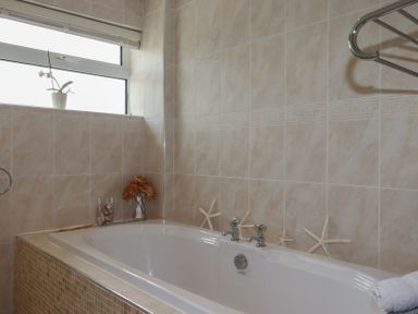 A bathtub with starfish decorations on beige tiled walls and a small window with a potted plant at Coastmans Nest in Mawgan Porth