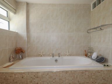 A bathroom with a built-in bathtub surrounded by beige tiles with starfish and towels at Coastmans Nest in Mawgan Porth