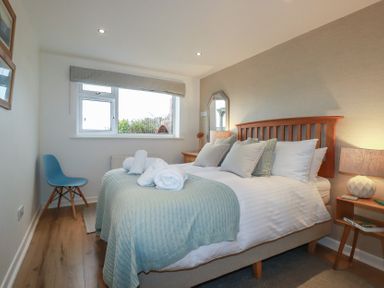 A bedroom with a bed with pillows and folded towels bedside tables a blue chair and a window at Coastmans Nest in Mawgan Porth