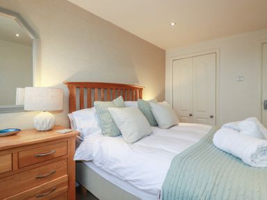 A bedroom with a wooden headboard bed pillows dresser lamp and folded towels at Coastmans Nest in Mawgan Porth