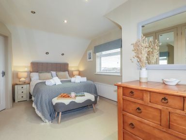 A bedroom with a bed bedside tables a bench a window and a wooden dresser with a mirror at Coastman's Nest in Mawgan Porth