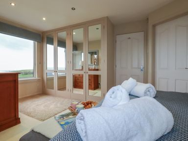 A bedroom with a bed showing rolled white towels breakfast tray with croissants and mugs a wooden chest of drawers mirrored wardrobe and two doors at Coastman's Nest in Mawgan Porth