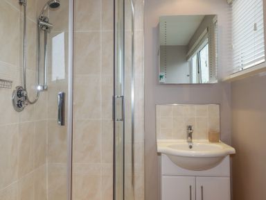 A bathroom with a shower enclosure and a sink with mirror and window blinds at Coastmans Nest in Mawgan Porth