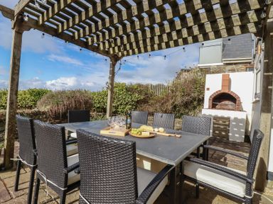 An outdoor patio with a dining table and chairs under a wooden pergola at Coastman's Nest in Mawgan Porth