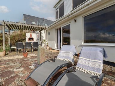 An outdoor patio with lounge chairs and a dining table under a pergola at Coastmans Nest in Mawgan Porth