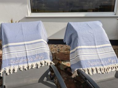 Two outdoor lounge chairs with blue and white striped towels on them outside a building at Coastmans Nest in Mawgan Porth