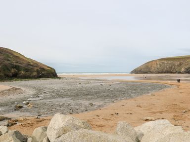 A sandy beach with rocks and hills on both sides and people walking near the water at Coastmans Nest in Mawgan Porth