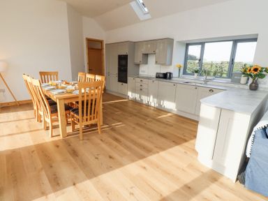 A kitchen with wooden dining table and chairs next to cabinets and a window at West Burton Hemmel in Bamburgh
