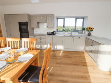 A kitchen with wooden dining table and chairs beige cabinets and a window with flowers at West Burton Hemmel in Bamburgh