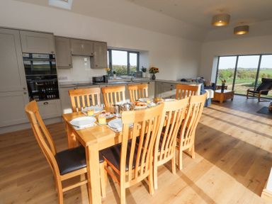 A dining area with a wooden table set for breakfast and kitchen cabinets in the background at West Burton Hemmel in Bamburgh