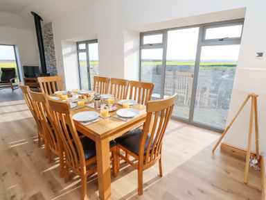 A dining area with a wooden table and eight chairs set with plates and glasses next to large windows at West Burton Hemmel in Bamburgh