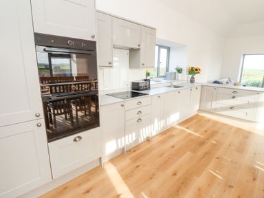 A kitchen with white cabinets a built in oven a toaster and sunflowers on the counter at West Burton Hemmel in Bamburgh