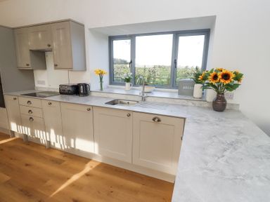 A kitchen with light grey cabinets a marble countertop a window above the sink and flowers on the countertop at West Burton Hemmel in Bamburgh