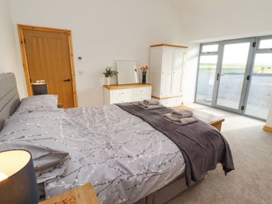 A bedroom with a bed towels bedside table dresser wardrobe and large glass doors at West Burton Hemmel Bamburgh