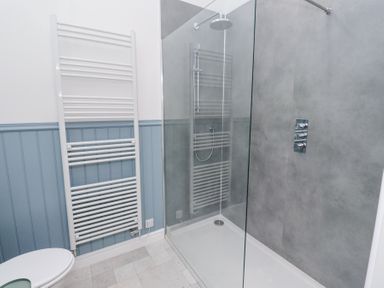 A bathroom with a walk-in shower, a white towel radiator, and blue paneling on walls at West Burton Hemmel in Bamburgh