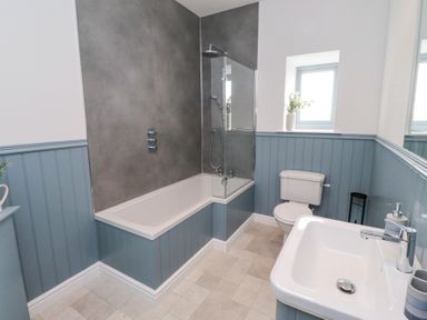 A bathroom with a bathtub shower combination a toilet a sink and a small window at West Burton Hemmel in Bamburgh