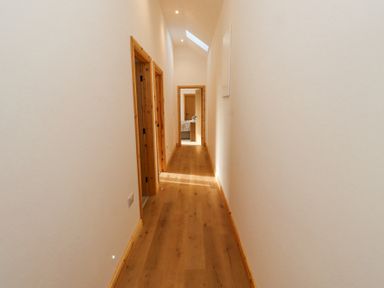 A narrow hallway with wooden flooring and door frames with doors leading to other rooms at West Burton Hemmel in Bamburgh