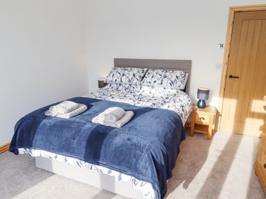 A bedroom with a double bed with floral bedding and a blue blanket next to a wooden door at West Burton Hemmel Bamburgh