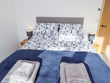 A bed with floral bedding and folded towels on a navy blue blanket between two wooden bedside tables with lamps at West Burton Hemmel in Bamburgh