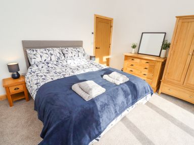 A bedroom with a bed covered in floral bedding and blue blanket with towels on top beside wooden bedside tables and drawers at West Burton Hemmel in Bamburgh