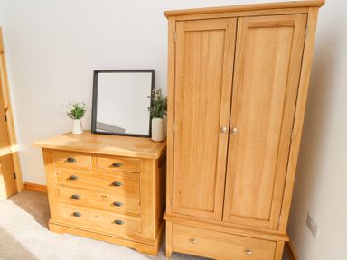 A bedroom corner with a wooden chest of drawers and a wooden wardrobe with a mirror and flower vases on the chest of drawers at West Burton Hemmel Bamburgh