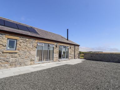 An exterior view of a stone house with solar panels at West Burton Hemmel in Bamburgh