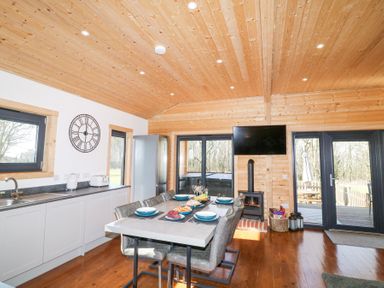 A kitchen dining area with a table set for six a wood stove a television and glass doors at Alpaca Lodge in Barkston