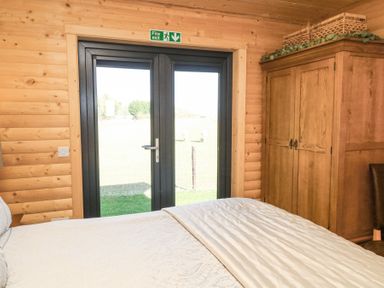 A bedroom with a bed a wooden wardrobe and glass doors with a fire exit sign at Alpaca Lodge in Barkston
