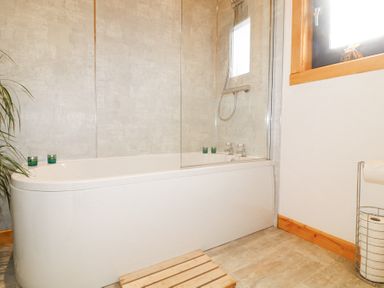 A bathroom with a bathtub a shower head candles a wooden bath mat and a window at Alpaca Lodge in Barkston