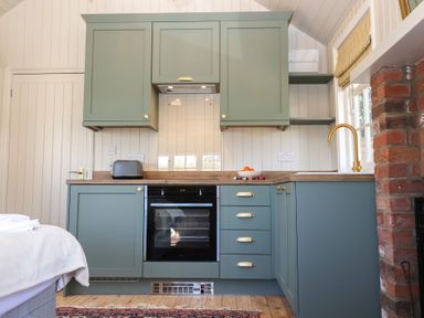 A kitchen with green cabinets a black oven a toaster a bowl of oranges and a gold faucet at The Woodshed in Tendring near Weeley