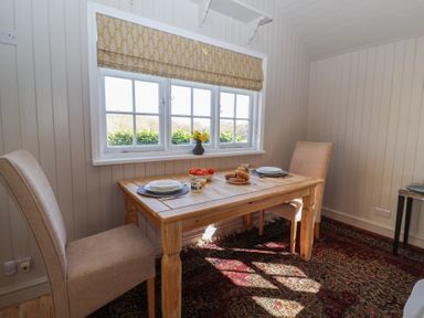 A small dining area with a wooden table and two chairs near a window with a patterned blind at The Woodshed in Tendring near Weeley