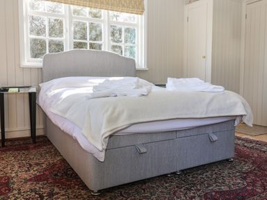 A bedroom with a bed with a grey headboard and white towels on it a side table and a patterned rug at The Woodshed in Tendring near Weeley