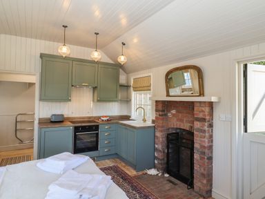 A kitchen with green cabinets a brick fireplace and folded towels on a table at The Woodshed in Tendring near Weeley
