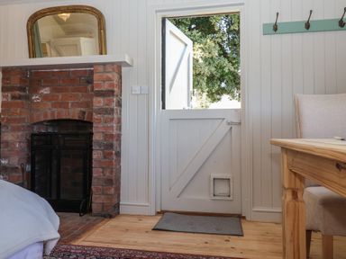 An interior room with a half open wooden door a brick fireplace and a wooden table with a chair at The Woodshed in Tendring near Weeley