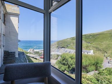 A view of the ocean and hill from a sunroom at Sea Ledge in Tintagel