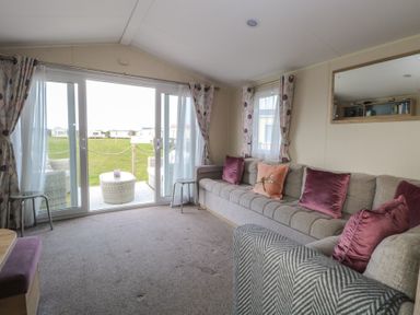 A living room with a large sofa and sliding glass doors leading to an outdoor seating area at Breathing Space in Happisburgh near Walcott