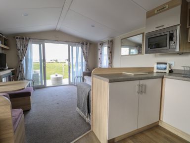 An open plan living area with kitchen cabinets a microwave a toaster a dining table with chairs and a sofa in Breathing Space Happisburgh near Walcott