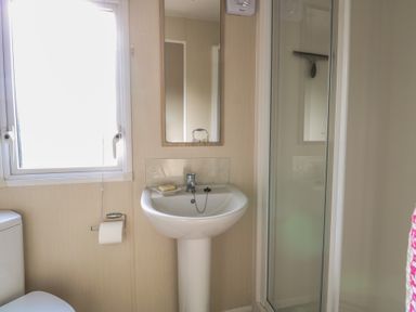 A bathroom with a pedestal sink a mirror a toilet a toilet paper holder a window and a glass shower enclosure at Breathing Space in Happisburgh near Walcott