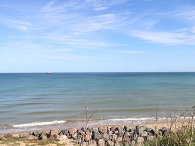 A beach with rocks and a calm sea with a boat in the distance at Breathing Space in Happisburgh near Walcott
