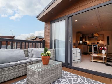A patio with wicker furniture and a potted plant outside a living room with a coffee table and kitchen at Lodge 36 - Kingfisher Lodge in Wickhamford near Evesham